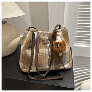 Detail of wool bucket bag with plaid pattern, leather strap and cute plush monster charm