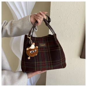 Detail of wool tartan bucket bag with leather handles and cute plush bear charm