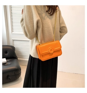 Chic orange leather crossbody bag with gold chain strap shown on a model in a modern room