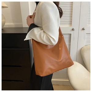 Detail of a large brown leather tote bag worn on shoulder by a model in home setting