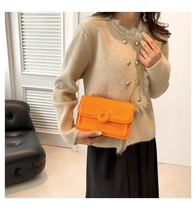 Detail of bright orange patent leather crossbody bag with elegant gold chain strap