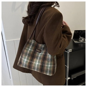 Detail of woolen bucket bag showing plaid pattern and leather logo tag on the front side