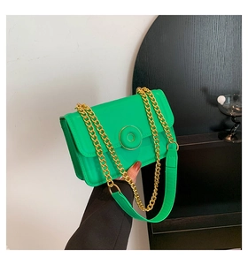 Detail of green faux leather crossbody bag with gold chain strap and round metal clasp