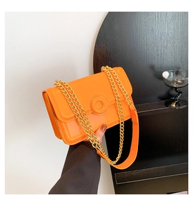 Close-up of bright orange crossbody bag with textured leather and gold chain strap