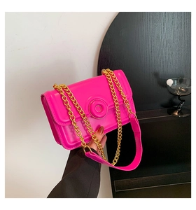 Detail of neon pink crossbody bag featuring gold chain strap and round buckle closure