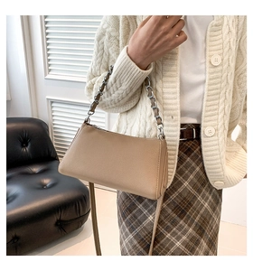 Detail of a beige PU leather crossbody bag with silver chain strap on a model