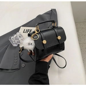 Detail van zwarte crossbodytas met gouden hardware en witte monster pluche hanger