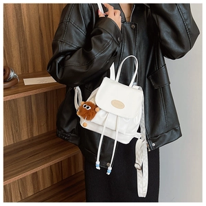 Close-up of white mini backpack with drawstring closure and cute plush monster charm