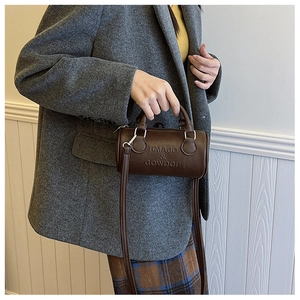 Borsa Boston in pelle marrone con logo a sbalzo indossata sopra un blazer di lana grigia