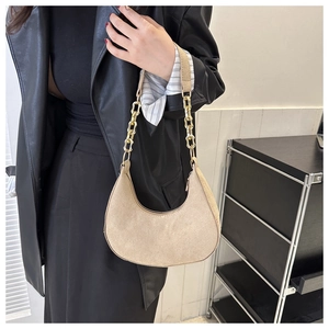 Detail of beige suede saddle bag with textured gold chain strap and moon-shaped silhouette