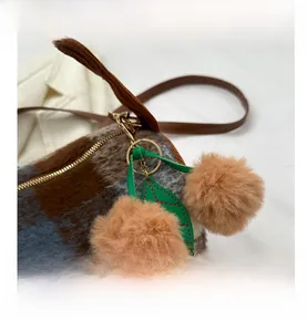 Detail der Pelz-Boston-Tasche mit Kirsch-Pompons und grünem Blatt-Anhänger am Reißverschluss