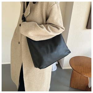 Close-up of a black pebbled leather hobo tote bag worn with a beige wool coat