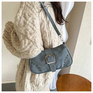 Detalle del bolso de hombro gris azulado con gran hebilla plateada y remaches metálicos