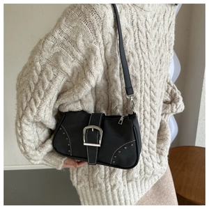 Detalle de bolso de hombro negro con hebillas plateadas y costuras blancas sobre un suéter