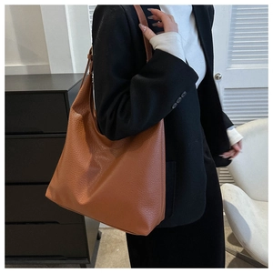 Close-up of brown litchi pattern leather tote bag with wide shoulder strap on model