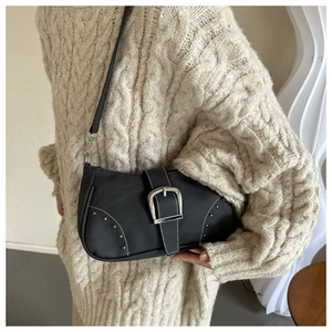 Detalle de bolso negro de hombro con hebilla plateada y remaches sobre suéter tejido