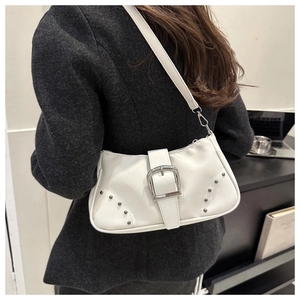 Detalle de un bolso de hombro de cuero blanco con hebilla plateada y remaches en una modelo
