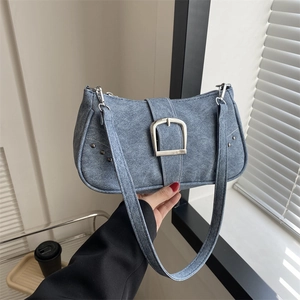 Bolso de hombro denim azul con hebilla plateada y remaches en un fondo minimalista