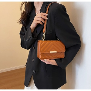 Detail of brown V-quilted chain shoulder bag with elegant gold metal bar and flap