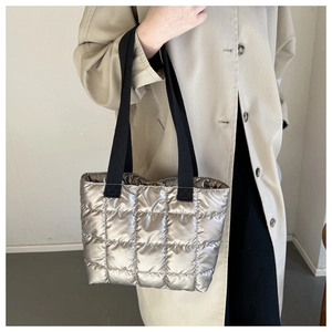 Detail of silver quilted tote bag on model wearing a beige trench coat in winter style