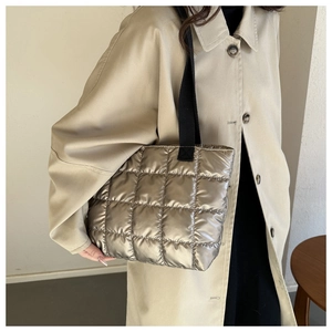 Detail of champagne metallic quilted puffer tote bag with black woven straps and soft texture