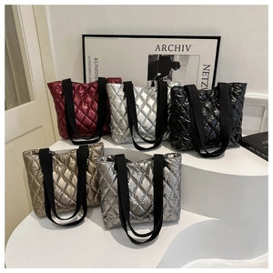Quilted metallic puffer tote bags in burgundy, silver, gold, and black on a white podium