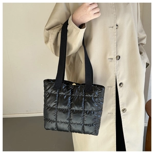 Detail of black quilted tote bag with wide straps and metallic magnetic closure