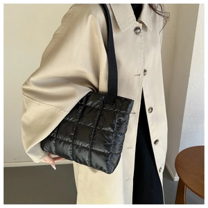 Macro detail of black quilted shoulder bag featuring glossy checkered padding and wide strap