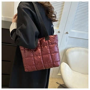 Close-up of quilted down tote bag in burgundy with metallic finish and wide black strap