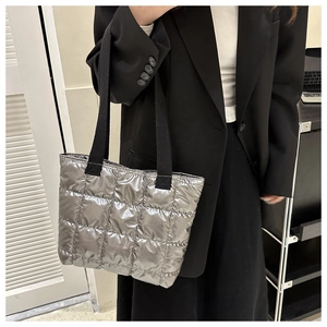 Close-up of a silver puffer tote bag with quilted nylon texture and black fabric straps
