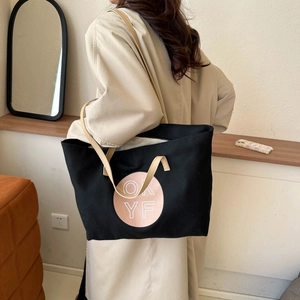 Black canvas tote bag with leather handles and pink OK YF print shown in a cozy interior
