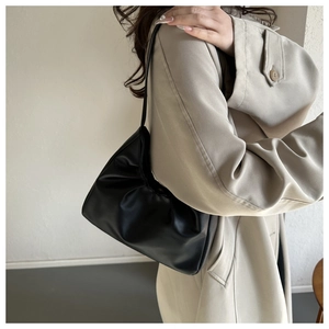 Detail einer schwarzen Falten-Cloud-Bag an der Schulter eines Models im beigen Trenchcoat