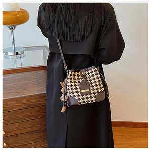Détail du sac seau à carreaux tissés avec garniture en cuir et pendentif ours sur modèle