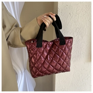 Close-up of wine red quilted tote bag with metallic glossy nylon and black canvas straps
