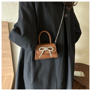 Détail d'un mini sac bandoulière marron avec nœud en strass et chaîne en métal