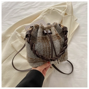 Detail of wool plaid bucket bag featuring a braided leather handle and gold hardware