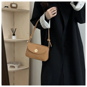 Detail of camel PU leather baguette bag with a golden turn-lock and knotted shoulder strap