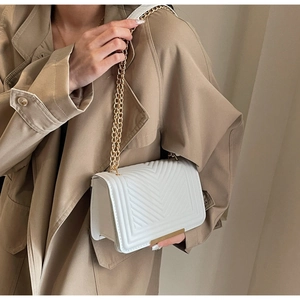 Detailed view of white quilted crossbody bag with gold chain strap and metal trim