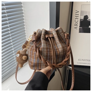 Detail of plaid wool bucket bag with brown woven handle and cute teddy bear charm