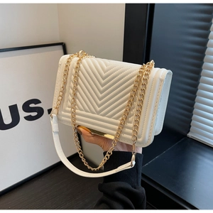 Macro detail of the white quilted leather texture and golden chain strap on this shoulder bag