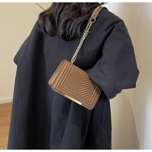 Detail of brown chevron quilted shoulder bag with gold chain strap on model back