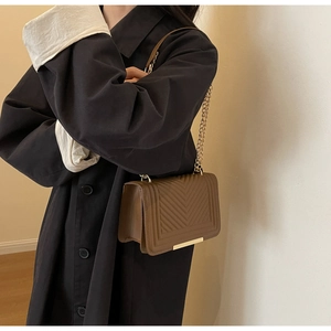 Detail of a brown quilted leather crossbody bag with elegant gold chain strap and stitching