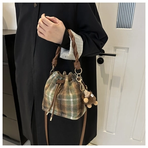 Detail of plaid drawstring bucket bag featuring wool fabric and a brown bear pendant