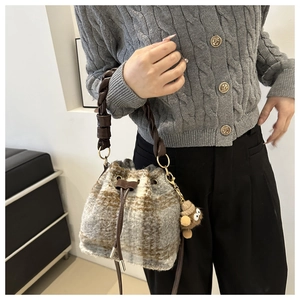 Close-up of a plaid textured bucket bag with drawstring and plush charm on casual outfit