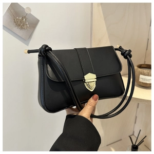 Detail der schwarzen Ledertasche mit goldener Schnalle und modisch verknotetem Schultergurt