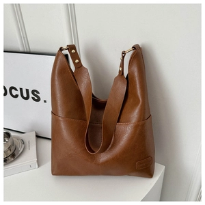Dettaglio di una borsa tote in pelle marrone con tracolla larga e rivetti dorati