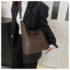 Dettaglio di una borsa a secchiello in pelle marrone con tracolla larga e parti metalliche dorate