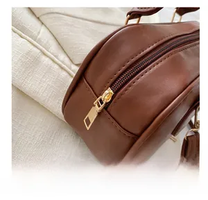 Detail of smooth gold zipper hardware and brown leather texture on a Boston bag