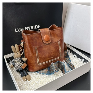 Detail view of brown bucket bag with patterned strap and bunny charm in gift box