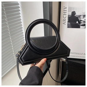Detail of black geometric PU leather handbag featuring a large circular ring handle and gold hooks
